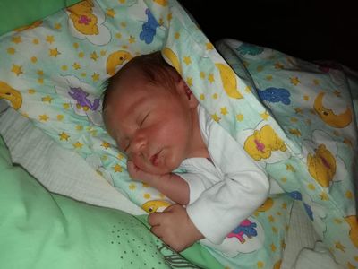 Ein Neugeborenes schläft friedlich unter einer Decke mit Zeichentrickfiguren und Sternen. Das Baby trägt ein weißes Langarmshirt.