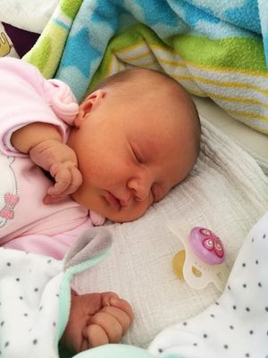 Ein Neugeborenes schläft friedlich, trägt ein rosa Outfit mit einem Cartoon-Charakter und liegt auf einer weißen Decke mit einer bunten Decke in der Nähe.