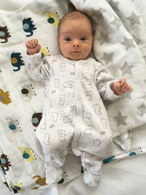 Ein Baby in einem weißen Overall mit Bären-Designs liegt auf einer Decke mit Sternenmustern.