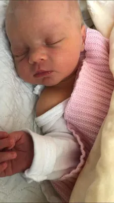 Ein Babymädchen schläft friedlich auf einer weißen Decke und trägt eine rosa gestrickte Decke und weiße Kleidung.