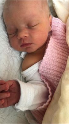 Ein Babymädchen schläft friedlich auf einer weißen Decke und trägt eine rosa gestrickte Decke und weiße Kleidung.