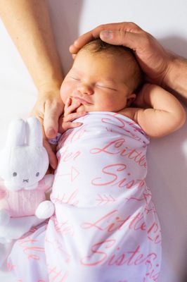 Ein Babymädchen schläft friedlich, eingewickelt in eine rosa Schlafsack mit der Aufschrift 'Kleine Schwester'. Sie hält einen weißen Miffy-Plüschtier.