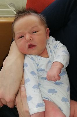 Ein Nahaufnahme eines Babys in blauen Wolken-Pyjamas, gehalten von einer Hand.