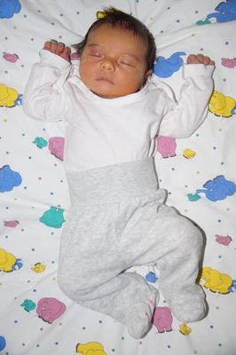 Ein Baby schläft auf einer bunten Decke mit Elefantendesigns, trägt ein weißes Shirt und graue Hosen.