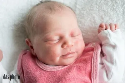 Ein schlafendes Babymädchen auf einer weißen Decke, mit einem rosa Lätzchen und weißen langen Ärmeln.
