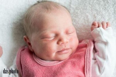 Ein schlafendes Babymädchen auf einer weißen Decke, mit einem rosa Lätzchen und weißen langen Ärmeln.
