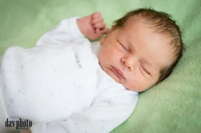 Ein Neugeborenes schläft friedlich auf einer grünen Decke. Das Baby trägt ein weißes Langarm-Bodysuit mit Sternen.