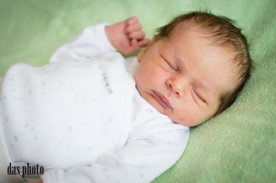 Ein Neugeborenes schläft friedlich auf einer grünen Decke. Das Baby trägt ein weißes Langarm-Bodysuit mit Sternen.