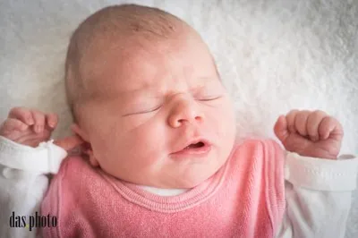 Nahaufnahme eines schlafenden Neugeborenen, das ein rosa Shirt und weiße lange Ärmel trägt, mit einer weißen Decke darunter.