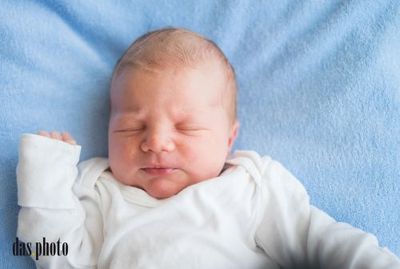 Ein Neugeborenes schläft auf einer blauen Decke und trägt ein weißes Langarmshirt. Die Augen des Babys sind geschlossen, und es sieht friedlich aus.