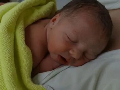 Ein Neugeborenes schläft auf einer grünen Decke, die um seinen Körper gewickelt ist. Die Augen des Babys sind geschlossen, und es scheint in einem friedlichen Schlaf zu sein.