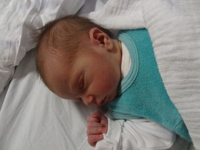 Ein Neugeborenes schläft friedlich auf einer weißen Decke und trägt ein blaues Lätzchen. Der Kopf des Babys ist leicht zur Seite geneigt.