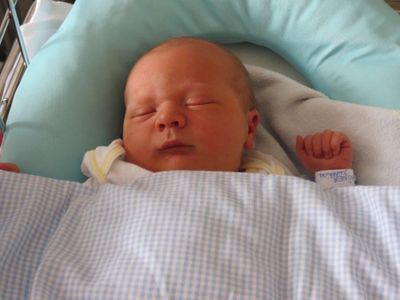 Ein Neugeborenes schläft friedlich in einem Krankenhausbett, eingewickelt in eine blau-weiß karierte Decke.