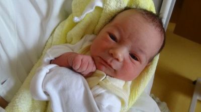 Ein Neugeborenes, in ein gelbes Tuch gewickelt, lächelt und schaut direkt in die Kamera.