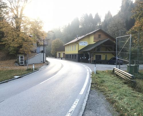 Eine ruhige Straße führt zu einem gelben Gebäude, wahrscheinlich einem Hotel, mit einem Auto davor geparkt. Das Gebiet ist von üppiger Grünfläche und Bäumen umgeben.