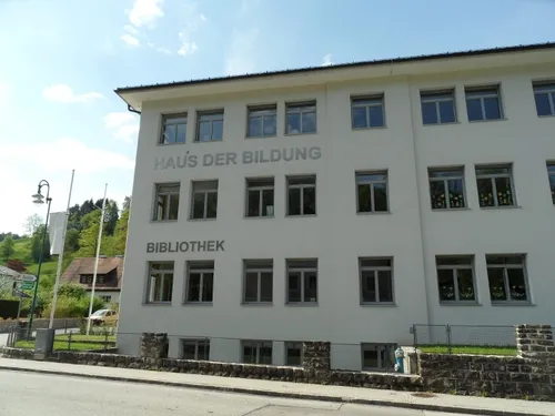 Ein großes weißes Gebäude mit der Aufschrift Haus der Bildung Bibliothek, vielen Fenstern und einem geparkten Auto davor.