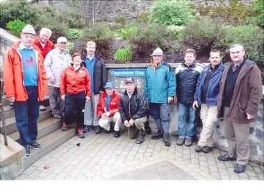 Eine Gruppe von Menschen, die für das Freie gekleidet sind, posiert für ein Foto auf einer Ziegelplattform, mit einem blauen Schild, das 'Copperthwaiter Steps' liest.