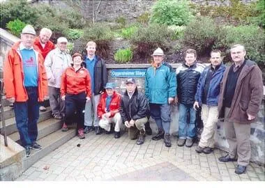 Eine Gruppe von Menschen, die für das Freie gekleidet sind, posiert für ein Foto auf einer Ziegelplattform, mit einem blauen Schild, das 'Copperthwaiter Steps' liest.