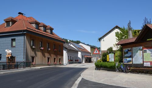 Eine sonnige Straße mit Häusern, Solarpanelen und Blumen. Ein Fußgängerübergangsschild und ein Fahrrad befinden sich auf der rechten Seite.