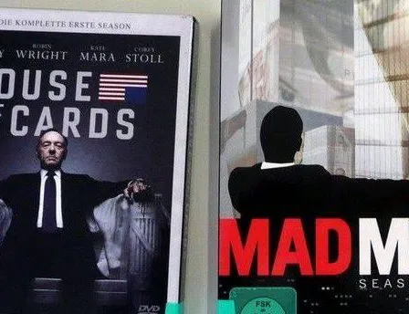 Zwei DVD-Cover sind zu sehen, eines für House of Cards und eines für Mad Men. House of Cards zeigt einen Mann in Anzug mit einer amerikanischen Flagge im Hintergrund. Mad Men zeigt einen Mann in Anzug mit verschwommenem Stadthintergrund.