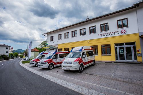 Drei Krankenwagen sind vor einem gelben Gebäude mit der Aufschrift 'Samariterbund Frankenfels' geparkt. Ein bewölkter Himmel thront darüber.
