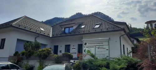 Das Arztezentrum Frankenfels Gebäude mit einem Ziegeldach und Fenstern ist von Grün umgeben. Ein Schild steht vor dem Gebäude mit den Namen der Ärzte und ihren Fachgebieten.