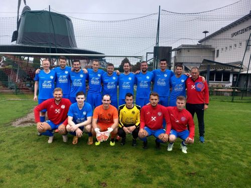 Eine Fußballmannschaft in blauen, gelben und roten Trikots posiert für ein Gruppenfoto vor einem Tor mit Netz.