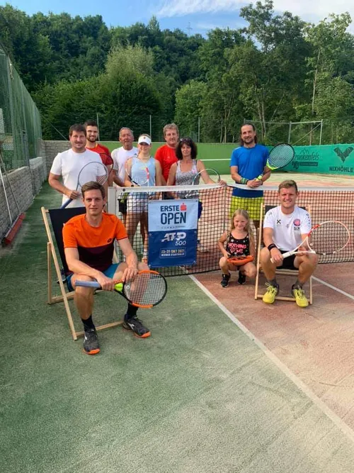 Eine Gruppe von Tennisspielern posiert für ein Foto auf einem Tennisplatz, mit einem Banner hinter ihnen, das 'Erste Open' steht.