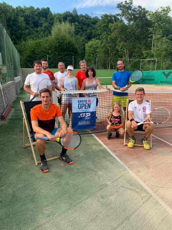 Eine Gruppe von Tennisspielern posiert für ein Foto auf einem Tennisplatz, mit einem Banner hinter ihnen, das 'Erste Open' steht.