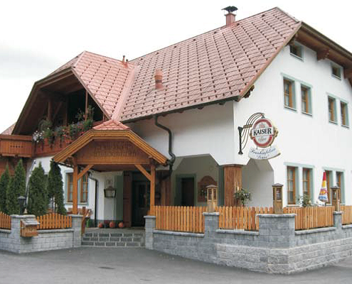 Ein weißes Gebäude mit einem roten Dach und einer Holzveranda. Der Eingang ist mit einem Holzzaun geschmückt. Das Schild steht 'Kaiser'.