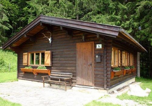 Ein Holzhaus mit einer Holzbank davor, Holzfenstern und einer Holztür mit einem Briefkasten darüber. Hirschgeweihe sind über der Tür angebracht.