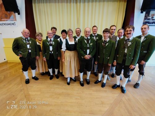 Zwölf Personen in traditioneller Kleidung posieren für ein Foto auf einem Holzboden. Ein Vorhang und Wasserzeichen sind vorhanden. Datum: 2021.8.29.