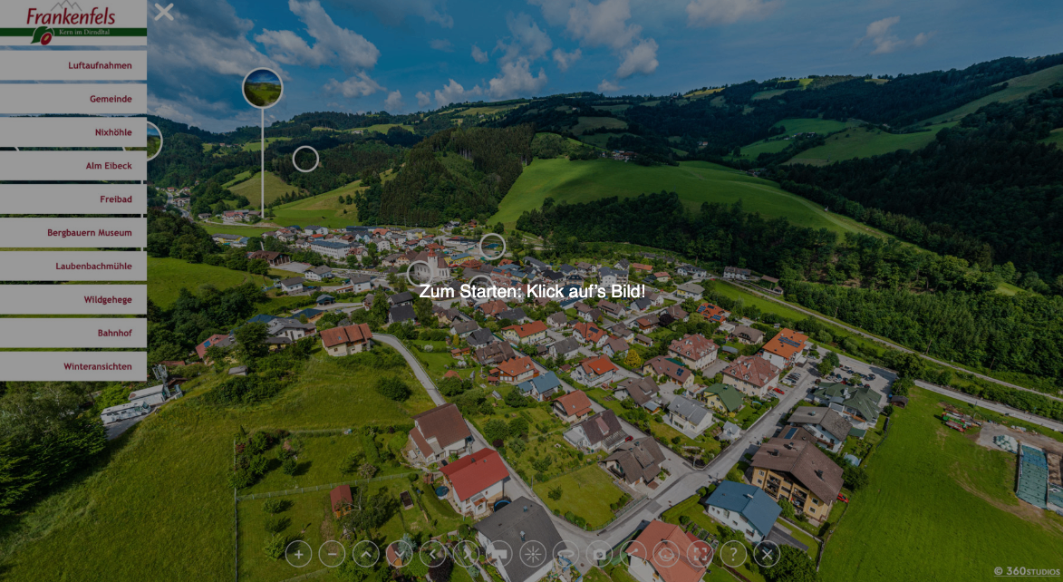Luftaufnahme eines Dorfes mit grünen Hügeln und Häusern, klicke um zu beginnen.