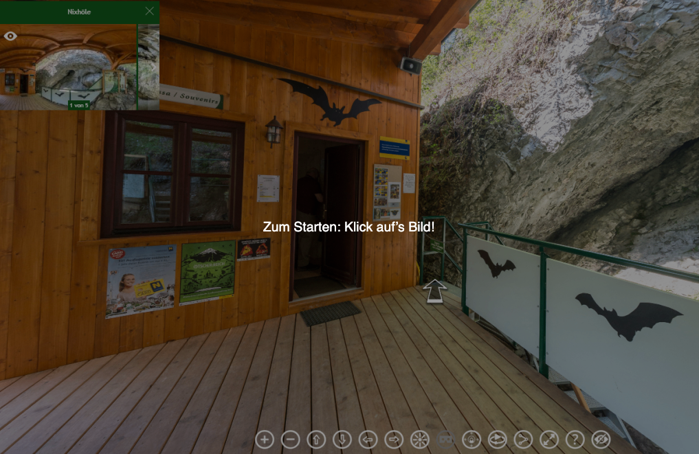 Ein hölzerner Eingang mit einem Fledermaus-Logo. Ein Mann steht am Eingang. Ein Poster und ein Fledermaus-Logo an der Wand. Ein Balkon mit Geländer. Ein Berg und ein Fledermaus-Logo an der Wand.