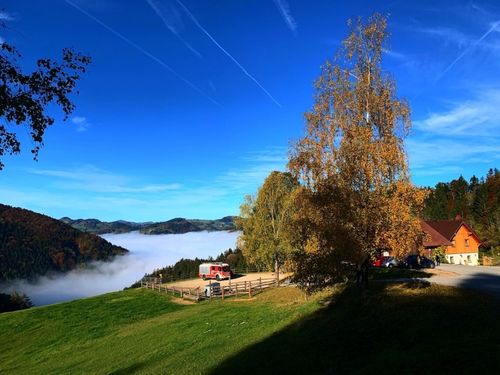 Ein Feuerwehrwagen auf einem Hügel mit Blick auf die Berge, den Nebel und eine Straße. Der Himmel ist klar und blau.
