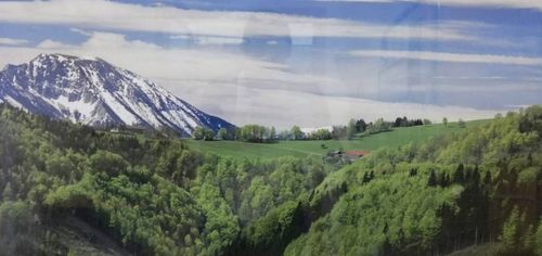 Ein schneebedeckter Berg, mit einem grünen Tal und einem kleinen Haus im Vordergrund.