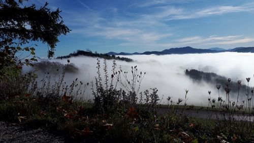Eine neblige Landschaft mit Bergen in der Ferne, einer Straße unten und einem blauen Himmel mit Wolken.