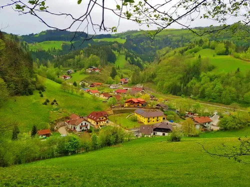 Luftaufnahme eines malerischen Tals mit vielen bunten Häusern, üppigen grünen Feldern und dichtem Wald.