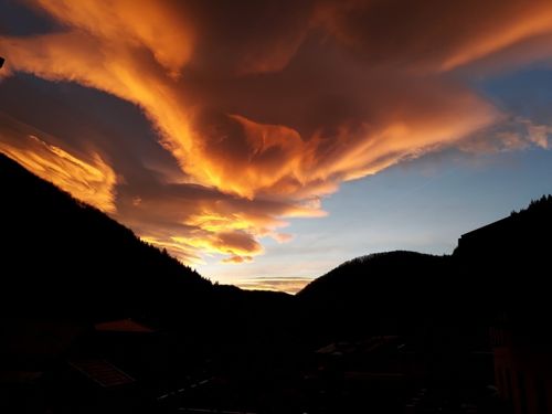Ein Sonnenuntergang über Bergen mit einem goldenen Himmel, gefüllt mit Wolken und einem Umriss von Hügeln unten.