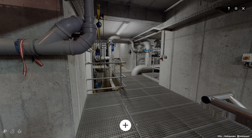 Ein Industriegebäude mit Rohren und Metallstrukturen, beleuchtet von einem hellen Deckenlicht. Eine Treppe führt in einen unteren Bereich.