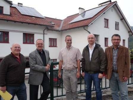Fünf Männer stehen vor einem weißen Haus mit Solarpaneelen auf dem Dach. Sie alle lächeln und scheinen für ein Foto zu posieren.