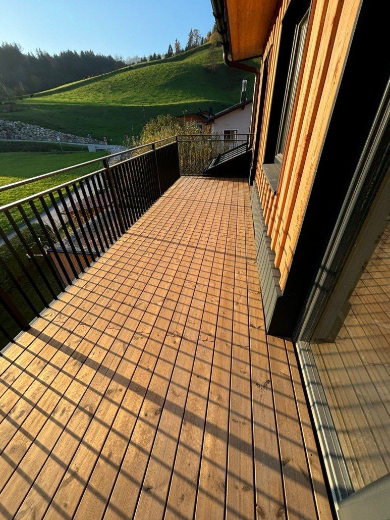 Eine Holzterrasse mit schwarzen Geländern und Blick auf einen grünen Hügel im Hintergrund.