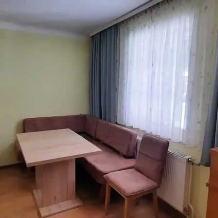 Eine gemütliche Ecke in einem Zimmer mit einem braunen Sofa, einem Holztisch und einem weißen Vorhang. Ein Heizkörper ist an der Wand montiert.