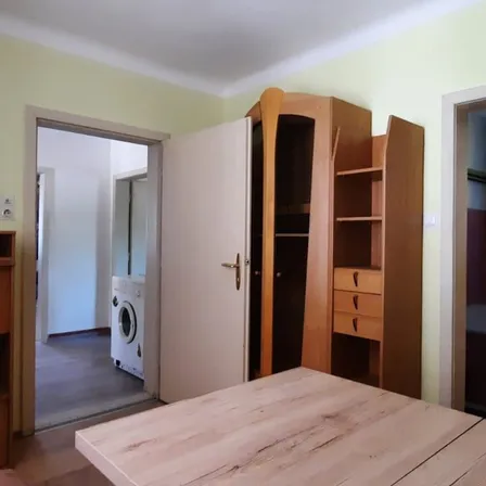 Ein leerer Raum mit Holzmöbeln, einer weißen Tür und einer Waschmaschine, die durch eine offene Tür sichtbar ist.