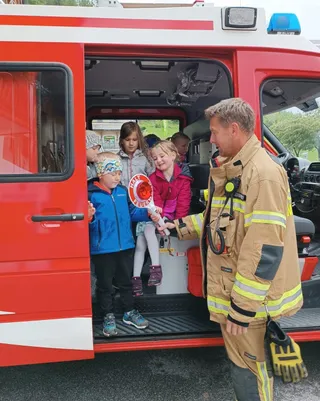 Ein Feuerwehrmann zeigt Kindern eine Feueralarmanlage und hilft ihnen, in einen Feuerwehrwagen zu steigen.