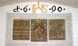 Ein gerahmtes Schild mit goldenem Text 'd.6.1990' über drei Tafeln mit altem Text, eine zentrale mit einem Bild eines gekrönten Mannes.