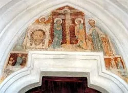 Ein Fresko mit religiösen Figuren, darunter Jesus am Kreuz, Maria und Heilige, schmückt den Bogen über einer Tür in einer Kirche.