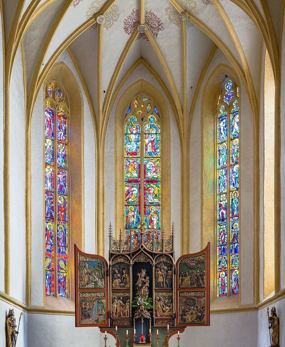 Ein Bild des Inneren einer Kirche mit einem hölzernen Altar und bunten Buntglasfenstern.