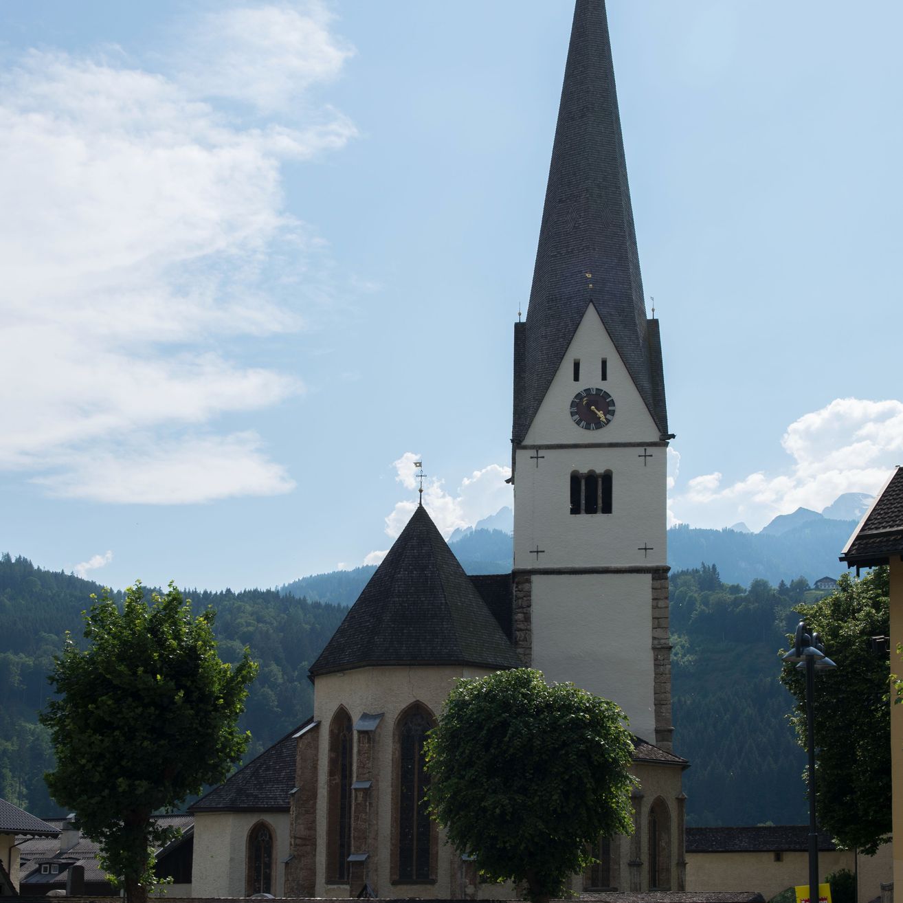 Eine alte Kirche mit einem Glockenturm in der Mitte eines Dorfes mit klarem Himmel und Bergen im Hintergrund.