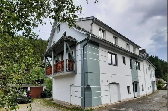 Ein weißes Haus mit grauen Streifen und einem Balkon hat ein Auto davor geparkt.